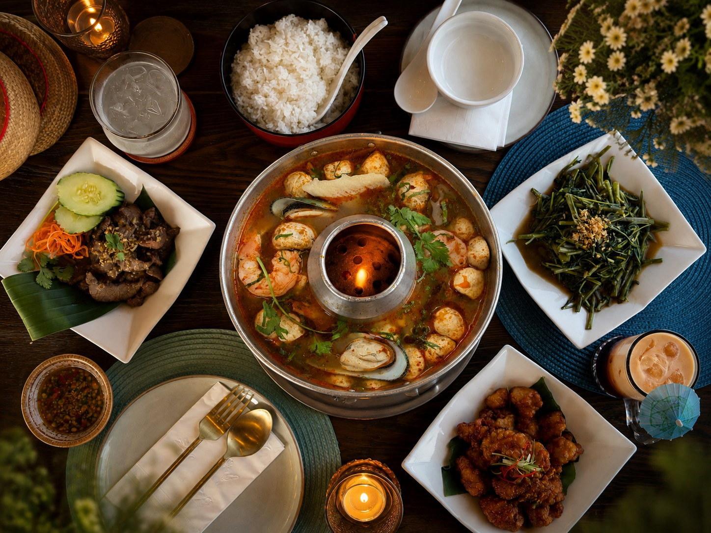 A family-style spread — tom yum seafood hot pot, crying tiger, orange chicken, morning glory and Thai iced tea