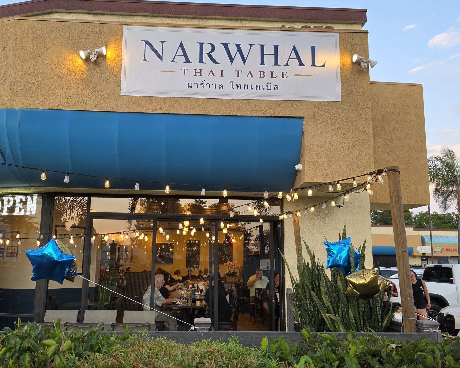 The Narwhal Thai Table storefront at dusk, string lights glowing over the patio